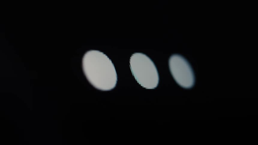 Three white dots light up one by one on a black screen in a macro close-up, representing a loading or typing animation
