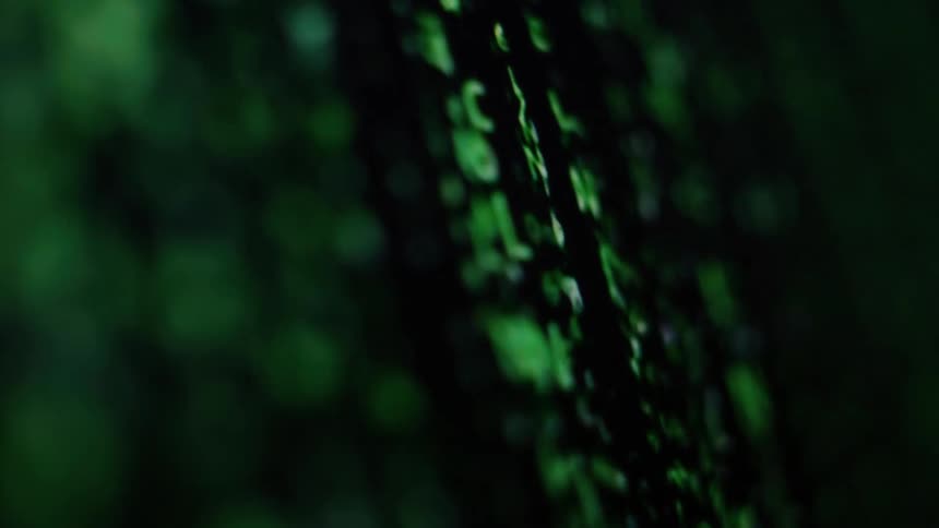 A macro, angled shot shows glowing green computer code and data streaming down a dark screen