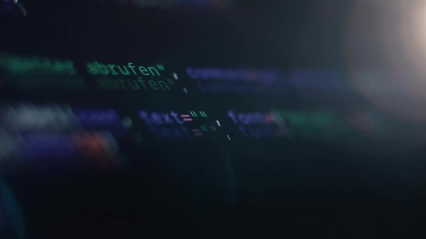 Lines of colorful computer code scroll down a dark monitor screen with a shallow depth of field