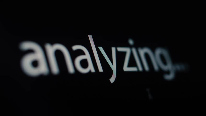 Macro close-up of the word "analyzing..." being typed onto a black computer screen, representing data processing
