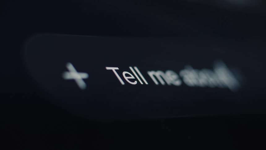 A macro close-up of a user typing 'Tell me about' into a search bar on a digital screen