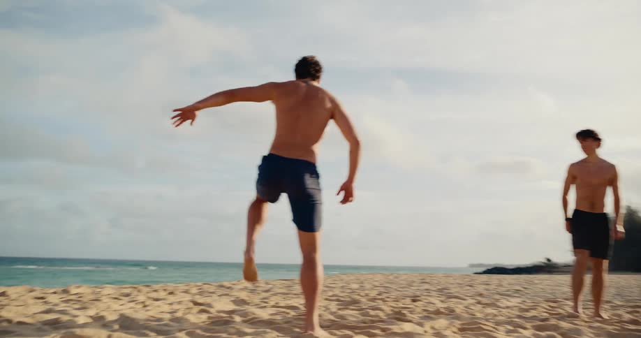 Young athletic friends have fun playing soccer together on a sandy beach in slow motion
