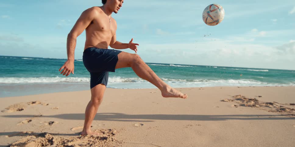 Slow motion shot of a man juggling a soccer ball on his foot at a beautiful sandy beach
