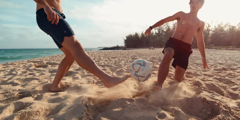 Two athletic young men in shorts play soccer on a sunny beach, captured in a dynamic super slow motion shot