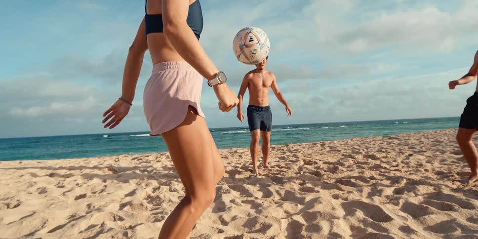 A group of young athletic friends expertly juggle a soccer ball on a sandy beach in a stunning super slow-motion shot