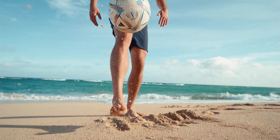 Cinemagraph of a man's feet and legs juggling a soccer ball on a sandy beach in super slow motion
