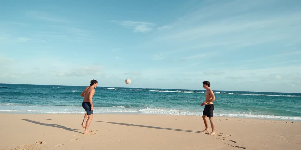 Cinemagraph loop of a young man juggling a soccer ball in super slow motion on a beautiful beach as his friend watches