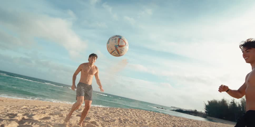 A young athletic man skillfully kicks a soccer ball into the air on a sandy beach in an epic super slow-motion shot