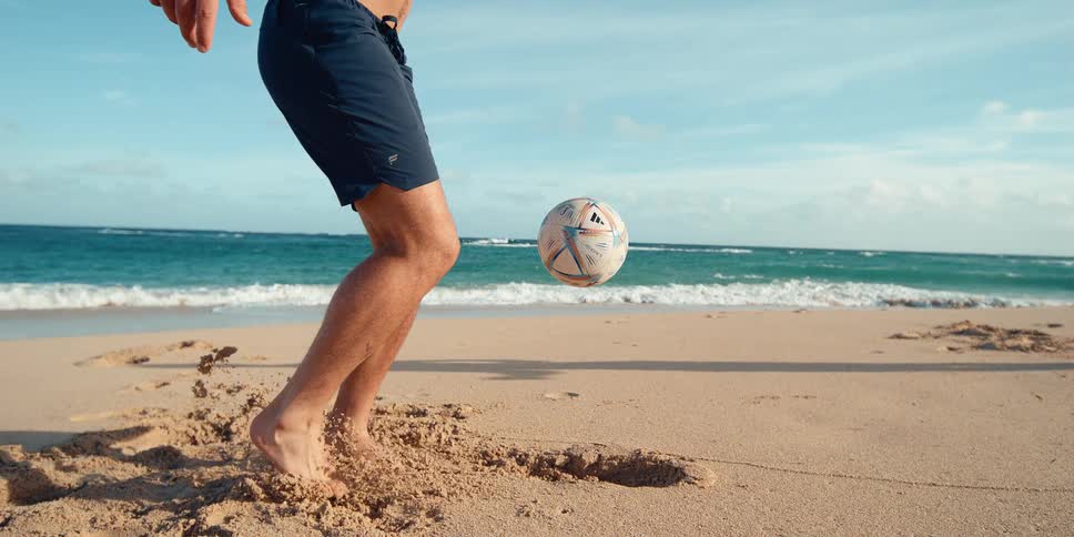Super slow motion close-up of a man skillfully juggling a soccer ball with his feet on a sandy beach