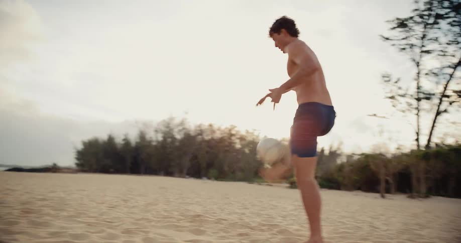 Two athletic young men skillfully juggle a soccer ball back and forth on a sandy beach during a beautiful sunset