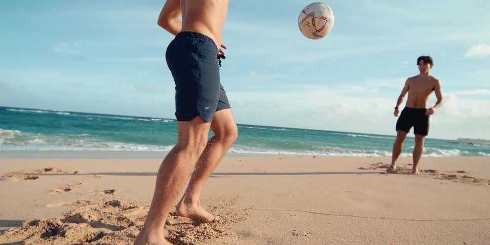 Two athletic men play soccer on a sunny beach as one skillfully juggles the ball in stunning super slow motion