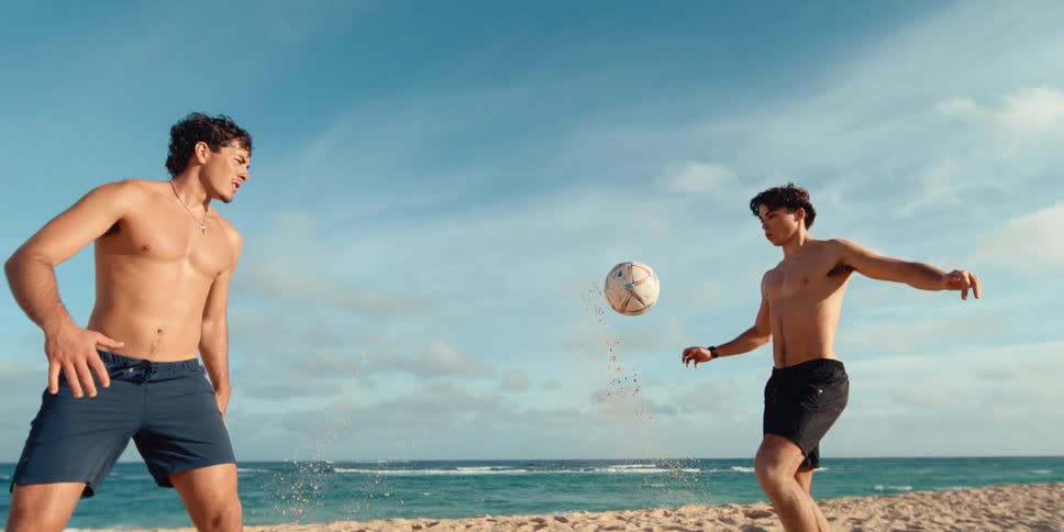 A young man kicks a soccer ball on the beach, captured in a stunning super slow-motion shot with sand flying everywhere