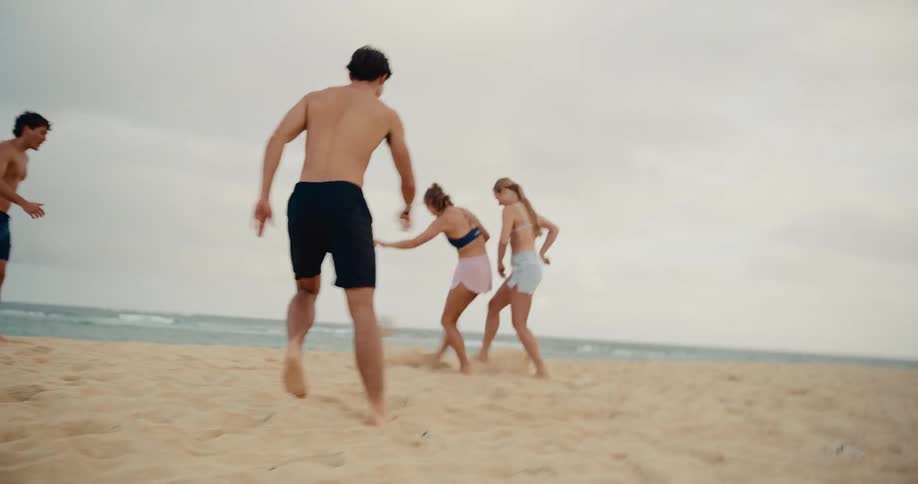 An energetic group of young friends have a blast playing a competitive game of soccer on the beach in slow motion