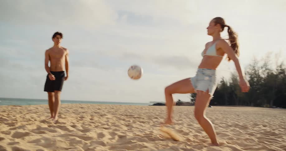 Athletic young friends have a blast playing a game of soccer on the beach in slow motion