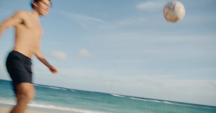 Two athletic young men skillfully juggle and pass a soccer ball on a beautiful sandy beach in slow motion