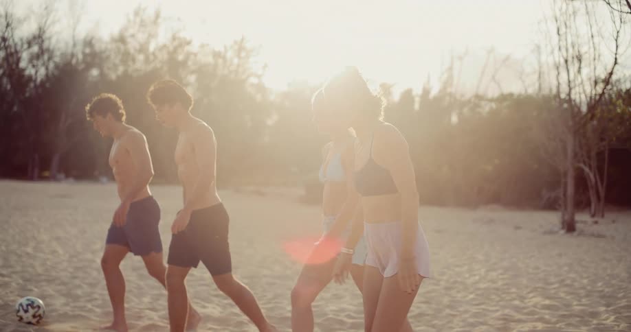 A group of friends practice soccer together on a sandy beach in slow motion at sunset