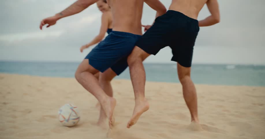 A group of energetic friends enjoys a competitive game of soccer on the beach in slow motion