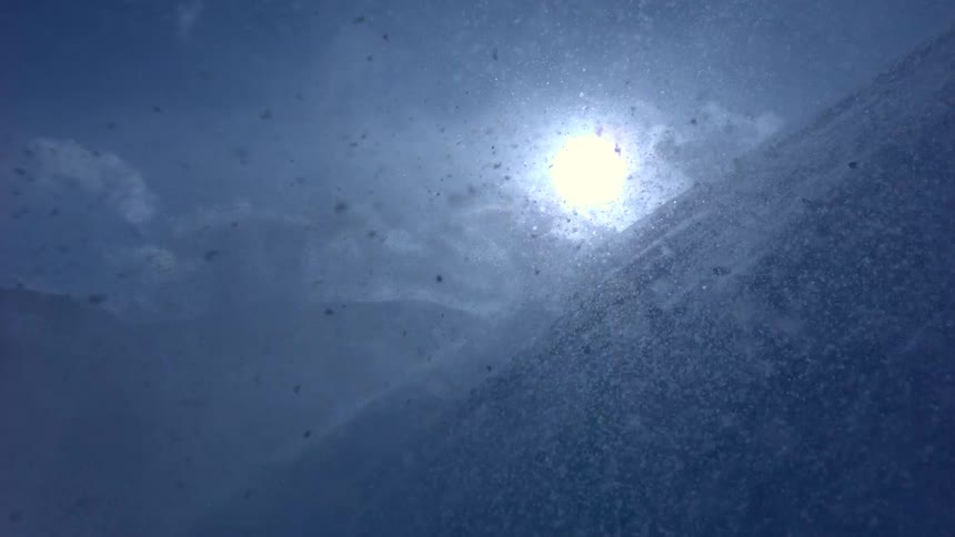 Dramatic slow-motion view from a snowy mountainside as a powerful blizzard rages under the bright sun