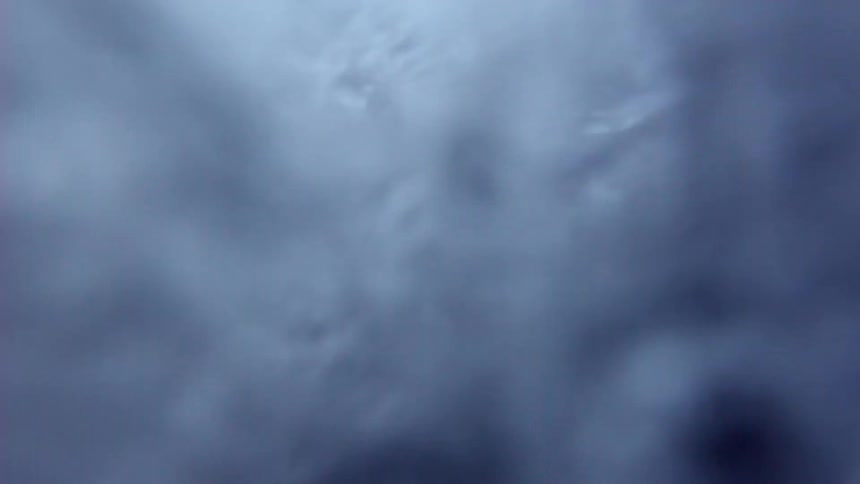 A dramatic super slow-motion close-up captures water bubbling and splashing against a dark surface before the camera is submerged