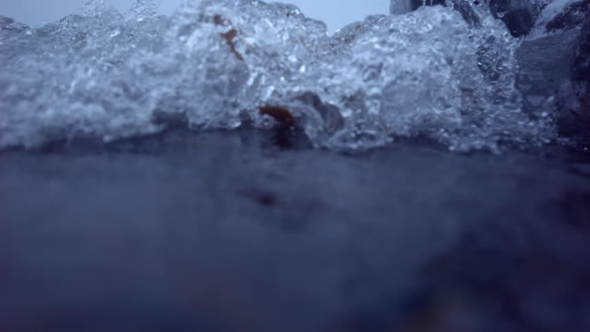 An extreme slow-motion close-up captures water splashing against icy rocks and gradually freezing over