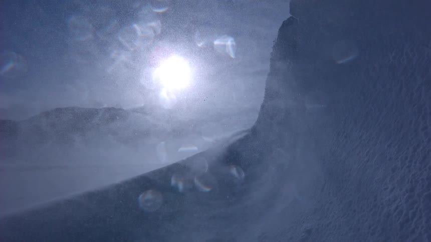 Wind whips snow across a frozen, sunlit landscape during an arctic blizzard