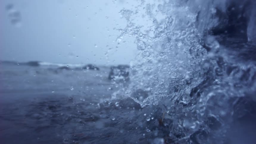 Extreme slow motion close-up of water splashing against an icy rock on a cold, overcast day