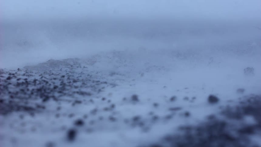 Fierce winds whip snow across a frozen and rocky landscape during an intense blizzard