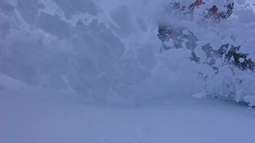 A dramatic super slow-motion shot captures a snowboard carving through deep snow, creating a massive wave of fresh powder
