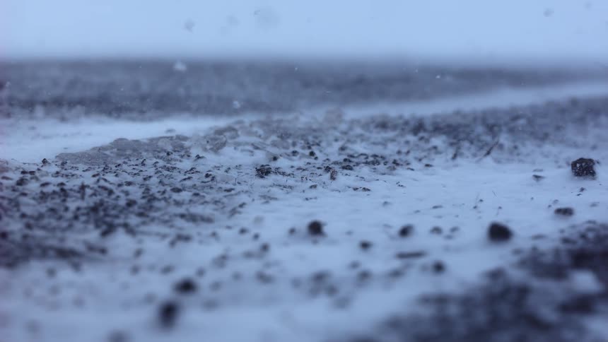 A close-up slow-motion view shows snow blowing across the frozen, rocky ground during a fierce winter blizzard
