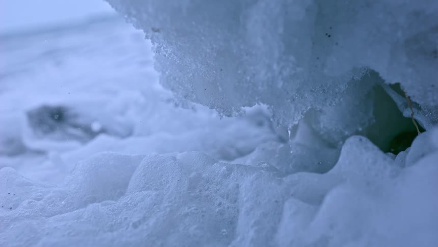 Extreme close-up of icy water splashing against an ice block and freezing into a foamy slush in super slow motion