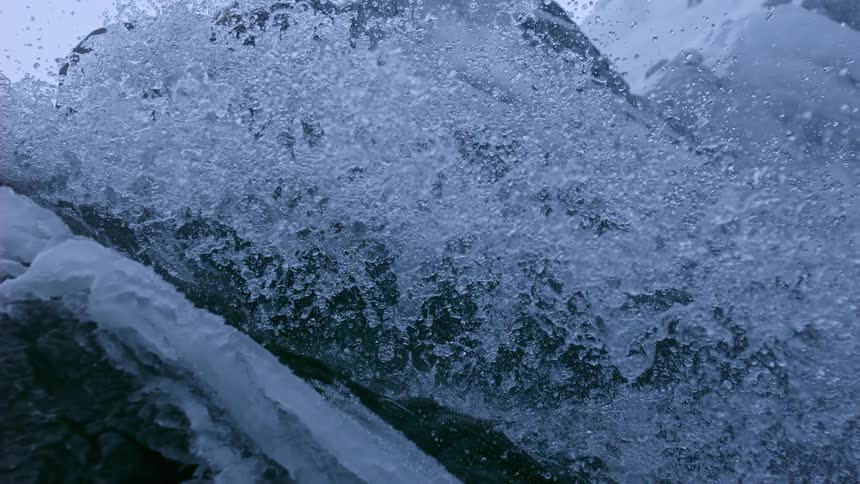 Super slow-motion close-up of a powerful winter waterfall cascading over icy rocks and snow
