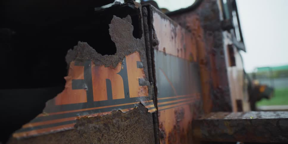 Close up detail shot of the decaying, rusted-through body of an abandoned orange lorry