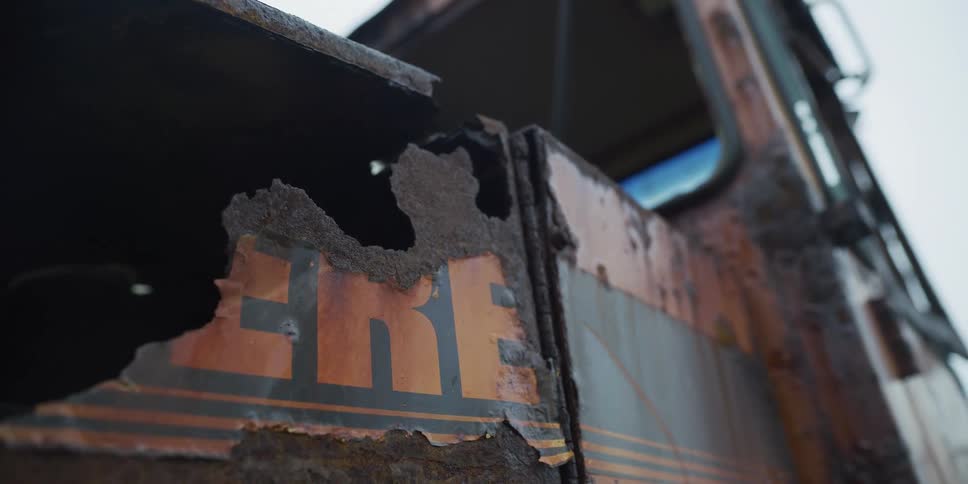 A low-angle close-up reveals the advanced decay and rust on an abandoned truck with a peeling logo