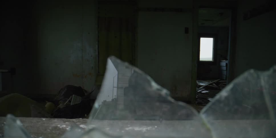 A desolate and spooky abandoned house is revealed in a slow-moving shot past shards of broken glass