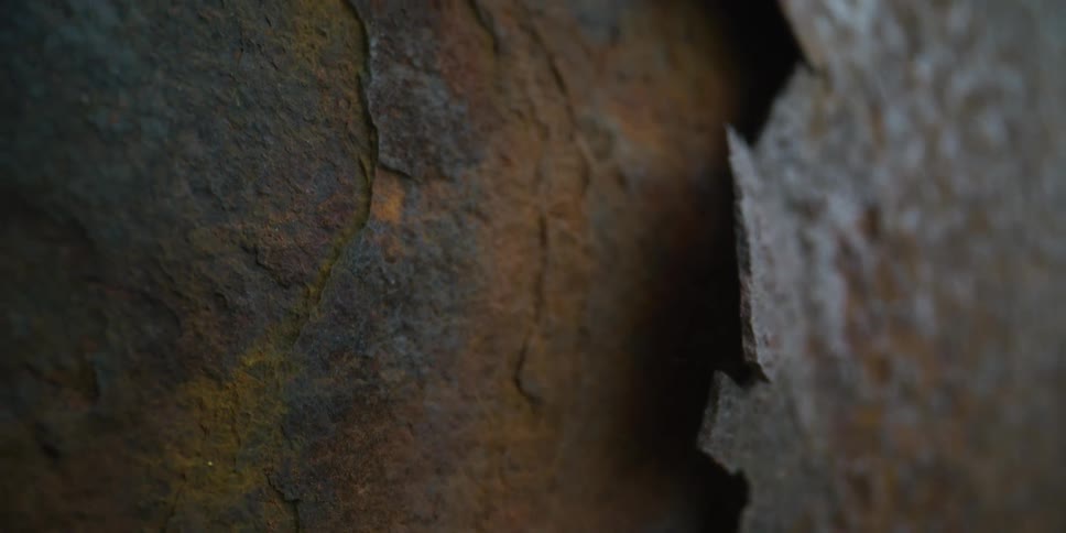 An extreme close-up dolly shot reveals the intricate textures of a decaying, rusted metal surface