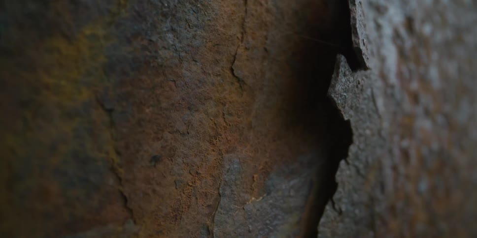 A close-up macro shot slowly pans across a heavily corroded and rusted metal surface, highlighting its weathered texture