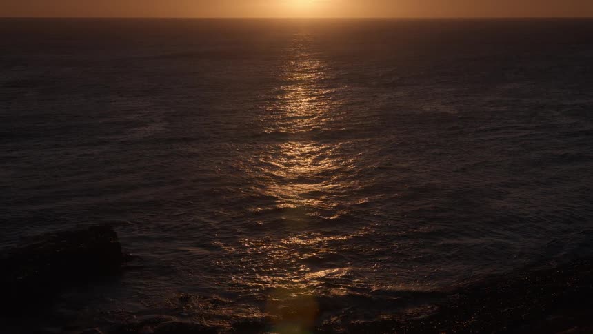 The golden light of the setting sun shimmers and reflects on the dark ocean waters