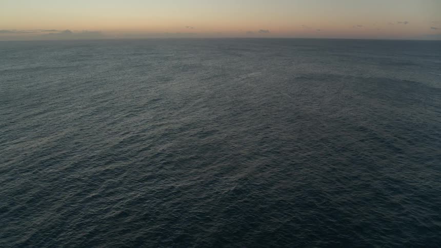A serene aerial view of the open ocean with calm, rippling water at sunset