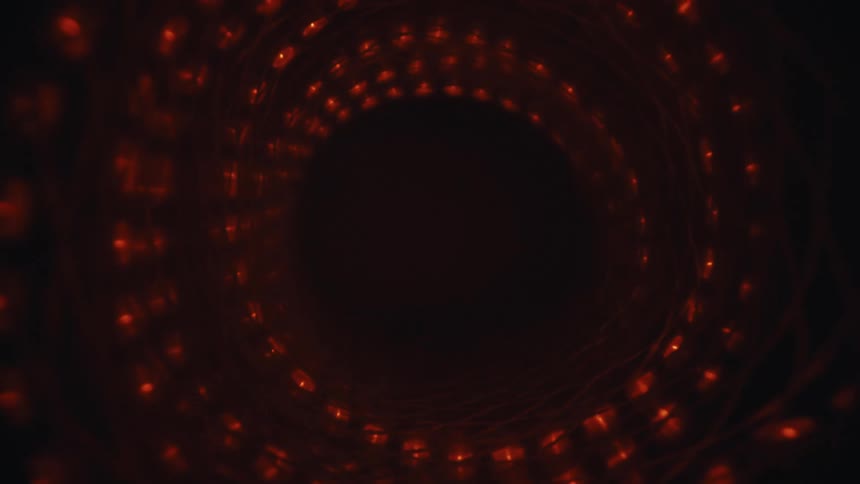 The camera slowly pulls back through a dark, abstract wormhole lined with pulsating red lights and swirling patterns
