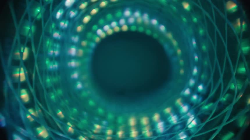 Slowly pulling back through a futuristic, spiraling tunnel of glowing green and blue LED lights that fades into darkness