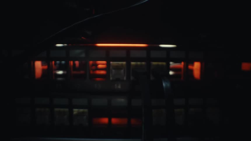 A macro shot pulls back as a hand plugs an ethernet cable into a glowing network switch in a dark server room