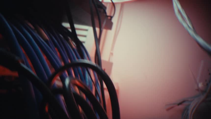 A dramatic close-up probe lens shot slowly moves through a tangled mess of wires and cables in a server room