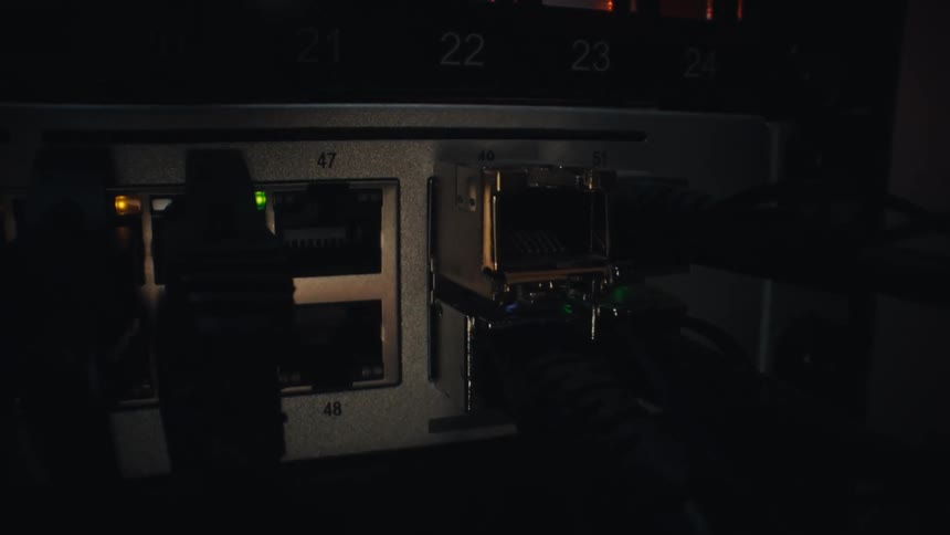 A slow push-in shot of blinking green LED lights on a network switch with ethernet cables plugged in, indicating data transfer in a dark server room
