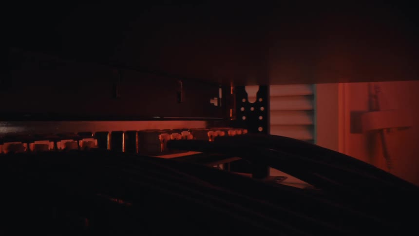 A mysterious macro shot dolly reveals network cables connected to a patch panel in a dark server room with dramatic red lighting