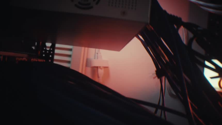 A slow revealing pan shot through a dark and cluttered server rack full of cables and wires