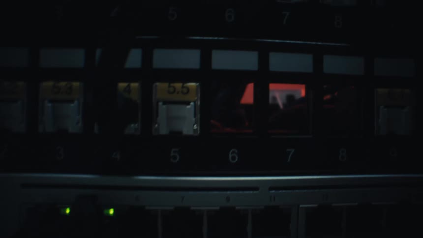 A close-up slow-motion pan of ethernet cables plugged into a network switch with blinking lights in a dark server room
