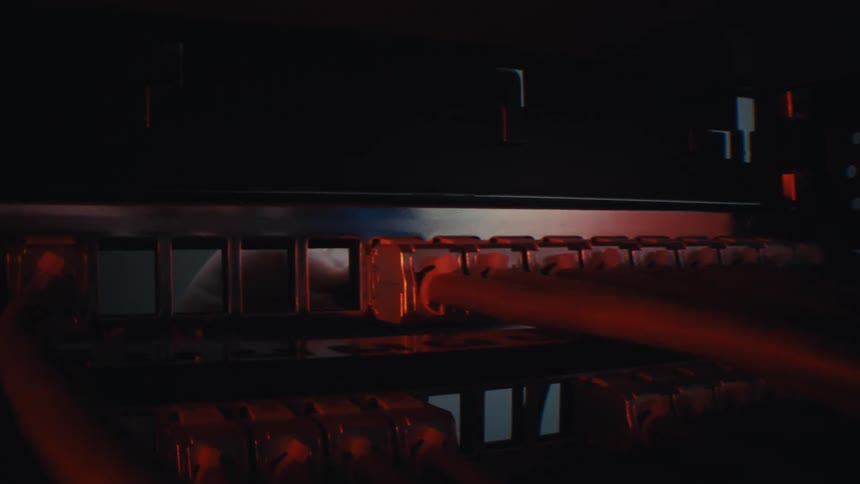 Close up of ethernet cables connected to a server rack port in a dark room with dramatic red lighting