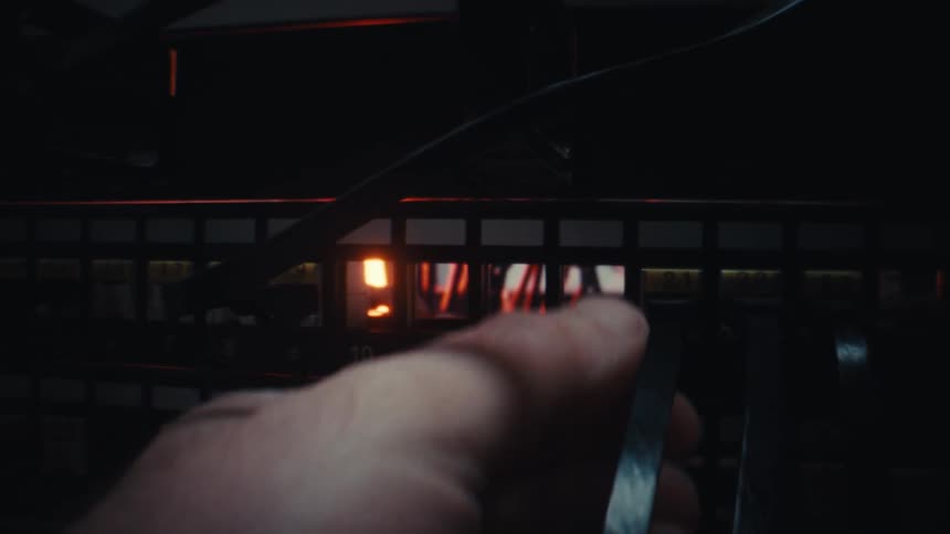 A person's hand slowly unplugs a network cable from a server rack in a dark data center