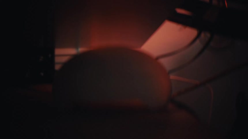 A shaky point-of-view shot moves through a dark, tangled mess of computer wires and electronic components under a desk