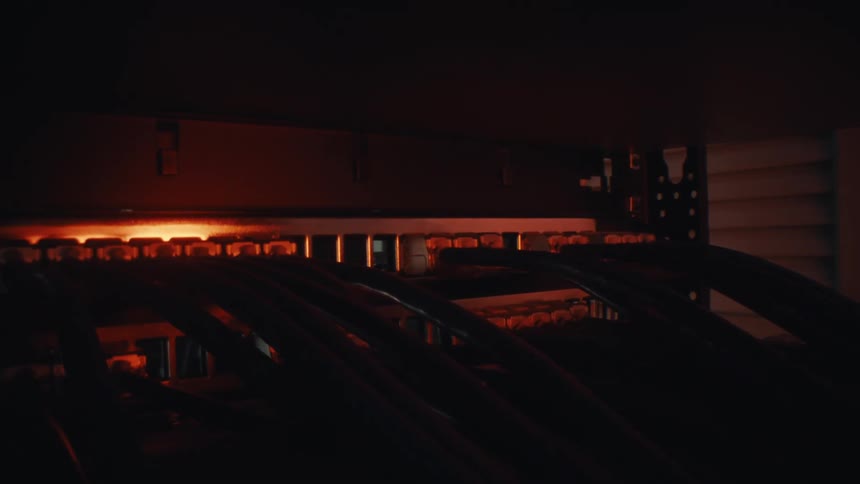 A dramatic close-up of network cables plugged into a server switch in a dimly lit, red-hued data center